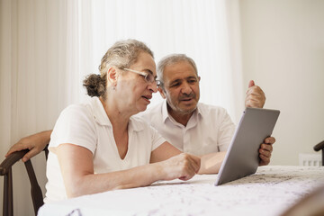 Happy senior couple wave having video call on laptop talking with relatives, smiling aged husband and wife sit on couch at home communicating via online using computer. Elderly and technology concept