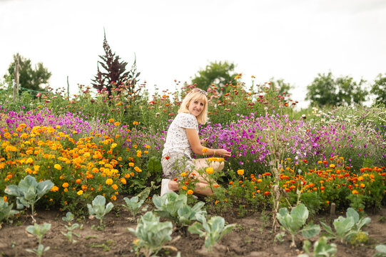 Happy girl sitting on a flower bed near the cabbage in the garden in a country house and posing for the camera with a smile on his face. Weekend work in the cottage