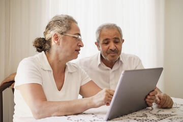 The elderly couple trying to use the tablet show each other something on the screen. old couple is trying to talk to their grandchildren. elders enjoying with benefits of technology