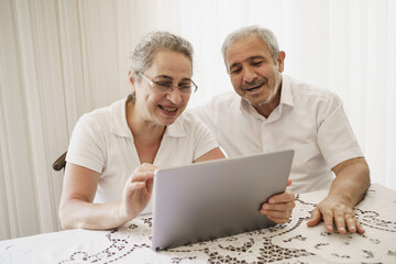 The elderly couple trying to use the tablet show each other something on the screen. old couple is trying to talk to their grandchildren. old couple is trying to talk to their children.