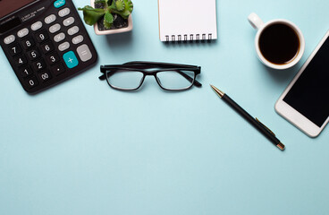 On a blue background are glasses, a calculator, a notebook, pens, a flower and a cup of coffee. Close-up business concept. Place to insert