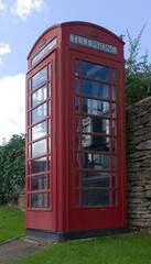 A traditional red telephone box in grass against a stone wall