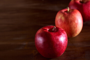 Three red apples lie on a cinnamon wooden table