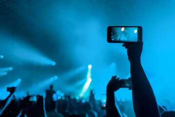 Fototapeta na wymiar A person films a concert on their smartphone. Hands close up. Rear view. Blue background. Concept of entertainment and modern technologies