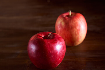 Two red apples lie on a cinnamon wooden table
