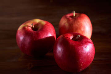 Three red apples lie on a cinnamon wooden table