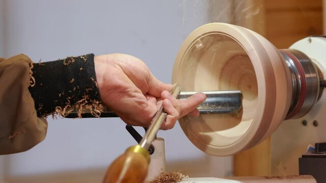 Craftsman works with workpiece in authentic workshop. Woodworker handles wood by bench. Making beautiful wooden handmade dish. Creation of unusual plate. Carpenter cuts wood by graver in soft focus