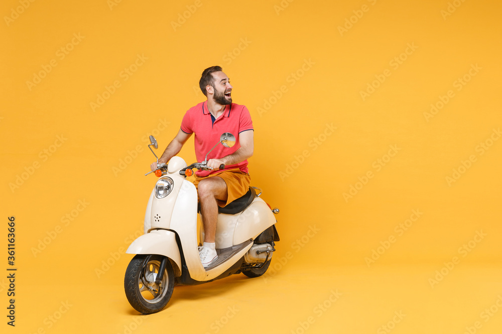 Wall mural cheerful young bearded man guy in casual summer clothes driving moped isolated on yellow wall backgr