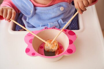 A child tastes with a wooden stick one rice Japanese roll