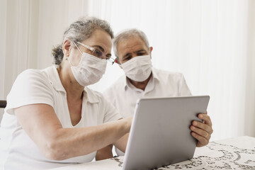 Senior couple wearing medical face mask and using tablet at home. quarantine. Corona Virus. order of products online and communicates on the Internet at home. stay home concept