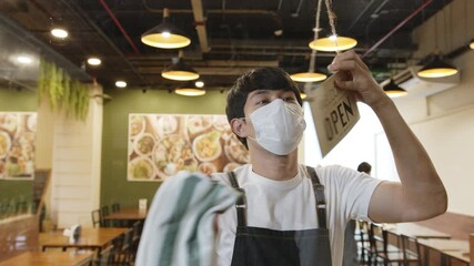 Business reopen again concept asian man working in a restaurant turning open sign at front to open after lockdown and epidemic of coronavirus covid-19 - Powered by Adobe