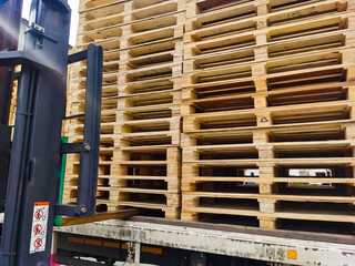 Worker driving forklift truck to unload wooden pallets stack from truck to the cargo warehouse to support shipment for logistics and transportation industry 