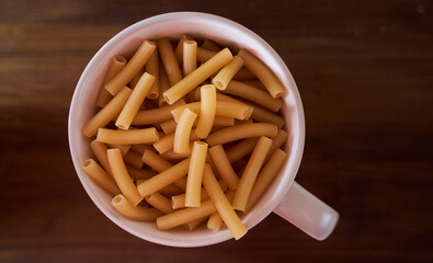 Yellow pasta lie in a white plate with a handle brown table. Close-up. Top view.