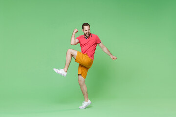 Happy young bearded man guy in casual red pink t-shirt posing isolated on green wall background studio portrait. People sincere emotions lifestyle concept. Mock up copy space. Doing winner gesture.