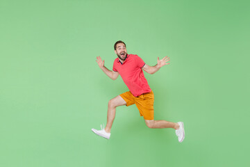 Fototapeta na wymiar Excited young bearded man guy in casual red pink t-shirt posing isolated on green wall background studio portrait. People emotions lifestyle concept. Mock up copy space. Jumping, spreading hands.