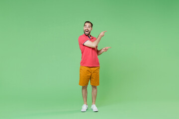Fototapeta na wymiar Excited young bearded man guy in casual red pink t-shirt posing isolated on green wall background studio portrait. People emotions lifestyle concept. Mock up copy space. Pointing index fingers aside.
