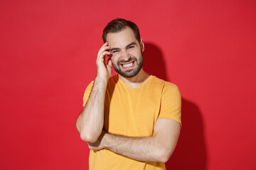 Displeased puzzled young bearded man guy in casual yellow t-shirt posing isolated on red background studio portrait. People sincere emotions lifestyle concept. Mock up copy space. Put hand on head.