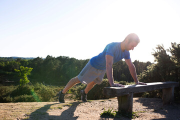 man doing press ups on a bench in the countryside