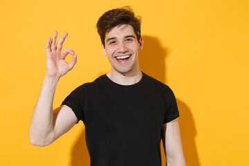 Cheerful young man guy 20s wearing casual black t-shirt posing isolated on yellow wall background...