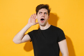 Shocked young man guy 20s in casual black t-shirt posing isolated on yellow wall background studio...