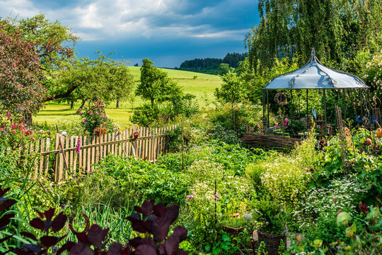 üppiger Bauerngarten mit Holzzaun und Pavillon, im Hintergrund Allgäuer Weiden und Streuobstwiesen D, Bodensee, Oberschwaben, Hinteressach