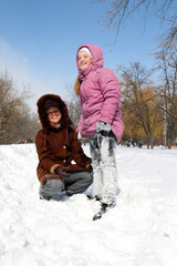 a small smiling girl in snow-covered pants with a smiling young woman squatting on the snow on a frosty day