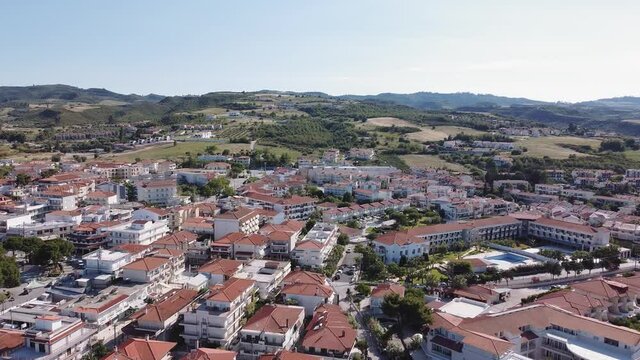 Chalkidiki, Greece coastal village 360 degrees landscape drone panning shot. Aerial view of Hanioti or Chaniotis at Kassandra peninsula with low rise buildings & clean tranquil blue sea.
