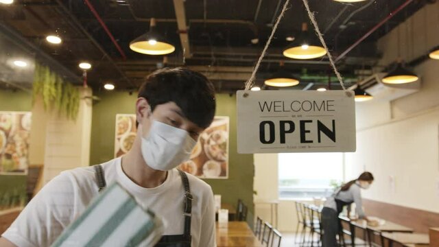 Business reopen again concept asian man working in a restaurant attach "keep distance" sign at front after lockdown and epidemic of coronavirus covid-19