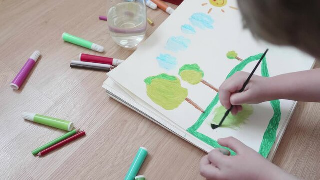 Child coloring a drawing of a field with a green watercolor