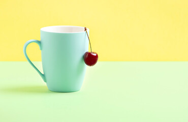 Sweet cherry on a blue mug, on a yellow and light green background.