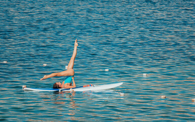 Young woman in blue swimsuite doing yoga on sup board with paddle. Balanced pose - concept of...