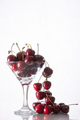 composition with cherry falling out of a full glass on a white background