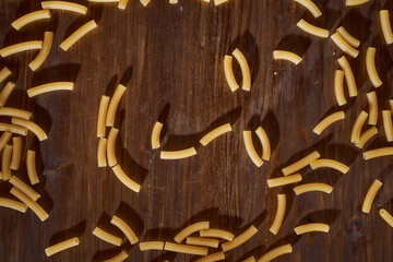Yellow pasta in a shape resembling a human face lies on a brown table. Close-up.