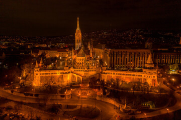 Fototapeta premium Aerial drone shot of Matthias Church with lights on Buda Hill in Budapest evening