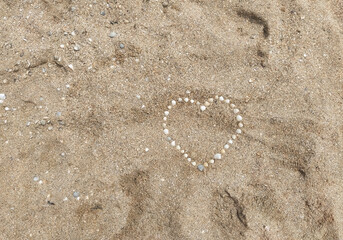 A large heart of seashells laid out on sea sand. Photograph, top view.