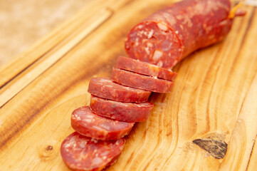 Close up view of a fresh sliced salami  placed on top of a wooden cutting board. Taken under a soft white light.