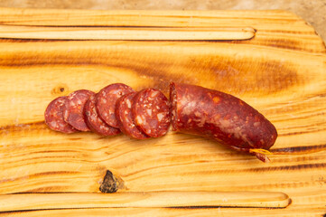 Close up view of a fresh sliced salami  placed on top of a wooden cutting board. Taken under a soft white light.