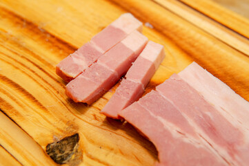 Close up view of few slices of bacon next to a bigger piece,  placed on top of a wooden cutting...