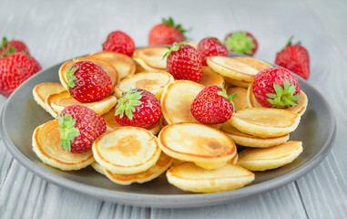 Small cereal pancakes with fresh strawberries in a plate on a wooden table. Fashionable comfortable food. European breakfast. Close-up.