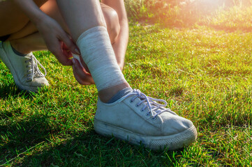 Young woman runner bandages her legs to protect tendons during long run and physical activity. Evening workout outdoors in the park
