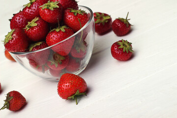 Red juicy and large strawberries in a glass bowl on a white table. Fresh summer fruit from the store.