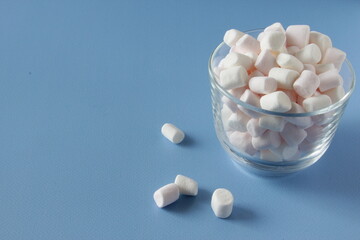 White Fluffy marshmallows in white cup isolated on blue background. Mini marshmallows. Winter food background concept.