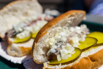 Typical traditional dutch herring sandwich close up macro shot with onions and green pickles and white bread 