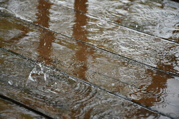 It is raining. Puddles on wooden flooring made of painted boards. Bouncing bizarre splashes. Circles diverge in water.