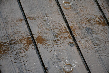 It is raining. Puddles on wooden flooring made of painted boards. Bouncing bizarre splashes. Circles diverge in water.