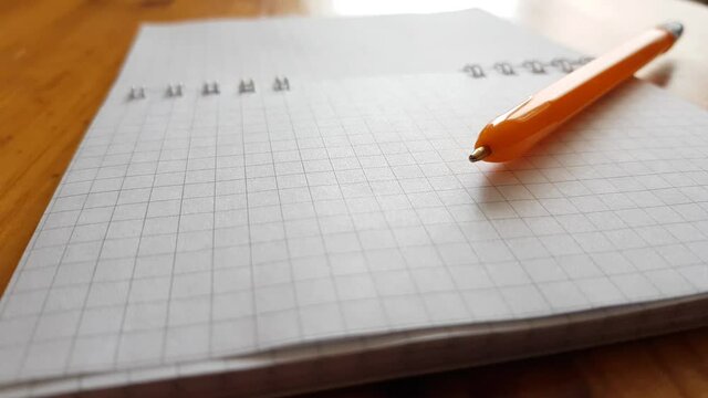 Orange ballpoint pen on a blank notepad paper, side view on a wooden table