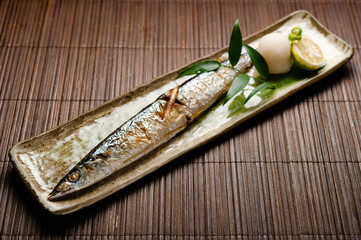 grilled whole mackerel fish with lime citrus and grated daikon radish on a long rectangler plate on...