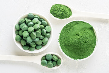 Chlorella or spirulina in the form of tablets and powder on a gray concrete background.