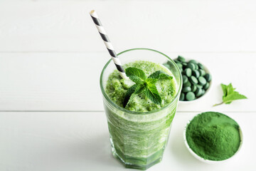 Glass of smoothies with addition of chlorella or spirulina with mint on a grey concrete background.