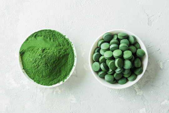 Chlorella or spirulina in the form of tablets and powder on a gray concrete background.